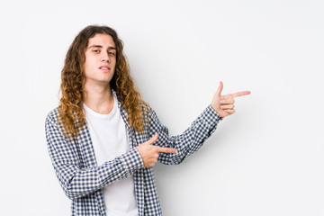 Wall Mural - Young long hair man posing isolated excited pointing with forefingers away.