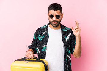 Wall Mural - Young latin man holding a suitcase crossing fingers for having luck