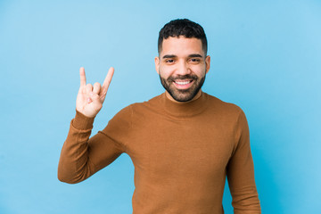 Wall Mural - Young latin man against a blue  background isolated showing a horns gesture as a revolution concept.