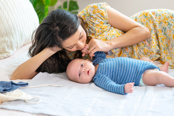 smiling caucasian mother holding hand and kissing her newborn baby son on the bed. mommy and cute in