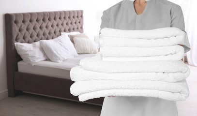 Poster - Chambermaid with clean folded towels near bed in hotel room, closeup