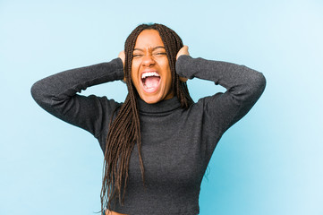 Young african american woman isolated on blue background covering ears with hands trying not to hear too loud sound.