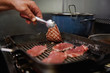 © Gabriel Trujillo/ADDICTIVE STOCK - Crop unrecognizable chef frying thin beef slices on grill pan on stove while showing delicious surface of meat using tweezers in kitchen