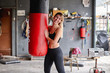 © Gabriel Trujillo/ADDICTIVE STOCK - Positive young sportswoman wearing leggings and sports bra hugging punching bag and looking away happily after intense workout in messy rural garage gym