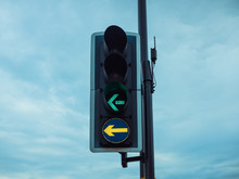 From Below Contemporary Traffic Light With Illuminated Green And Yellow Arrows Guiding To Left On Street In Cloudy Evening