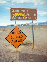 Temporary Road Sign With Bright ROAD CLOSED AHEAD Title And Sticker With CLOSED Inscription On Sign Indicating Names Of Destination Places With Mountains Far Away Under Cloudy Sky