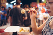 © Juan Alberto Ruiz/ADDICTIVE STOCK - Side view of crop ethnic female standing on crowded street in Zhubei Night Market and eating delicious fried dumplings from paper container