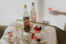 From Above Bottle Of Homemade Rose Wine Poured In Crystal Glass Near Champagne Trumpet And Served With Plate Of Fresh Raspberries And Blackberries Against White Wall With Hand Shadow