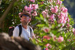 © Philippe Degroote/ADDICTIVE STOCK - Side view of hipster male tourist in stylish outfit with backpack standing near fence with blooming bushes and enjoying picturesque scenery of old town located among green hills in summer day
