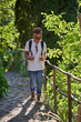 © Philippe Degroote/ADDICTIVE STOCK - Bearded hipster male hiker in stylish clothes and cap with backpack walking along wooden fence on narrow pathway in green forest in sunny summer day
