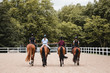 © Raquel Arocena/ADDICTIVE STOCK - Back view of company of female jockeys in uniform in saddles riding chestnut horses on sandy arena