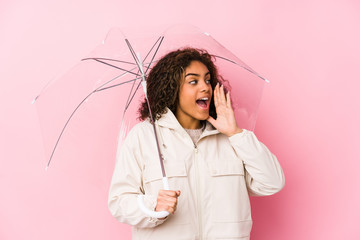 Wall Mural - Young african american woman holding a umbrella shouting and holding palm near opened mouth.