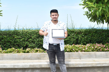 Indoor portrait of young man in t shirt standing against textured wall with copy space for ads, holding laptop and looking at camera with happy smile