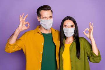 Poster - Close-up portrait of his he her she nice attractive healthy couple wearing safety mask health care insurance embracing showing ok-sign winking isolated violet purple color background