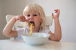 Portrait of adorable little blonde girl eating spaghetti for a lunch at home