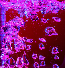 Close up view of the cold and fresh cola with bright bubbles in neon light. Texture of cooling summer's drink with macro bubbles on glass. Fizzing or floating up to top of surface, splashing fluid.