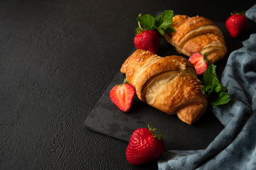 Wall Mural - Fresh golden croissants with strawberries on dark slate board. Top view