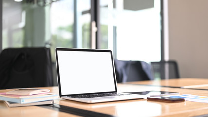 computer laptop with a white blank screen is putting on a meeting table surrounded by various equipm
