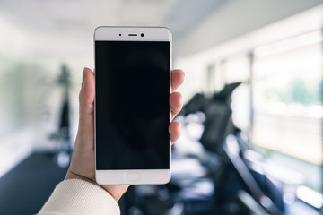 Woman hand with mobile phone in the gym opposite the sport equipment and  jogging simulators. Fitness app