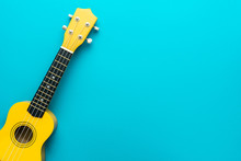 Top View Of Ukulele With Copy Space. Yellow Colored Wooden Ukulele Guitar On The Turquoise Blue Background.