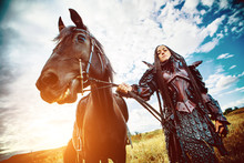 Girl In Medieval Knight's Armor With A Horse Against The Sunset Fields Background