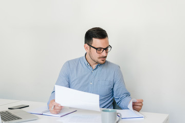 Portrait of serious young thoughtful confident businessman entrepreneur checking working plan and schedule or timetable in bright modern office copy space looking into data report information news