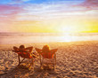 © Song_about_summer - happy couple on the beach vacation, holidays getaway travel, silhouettes of man and woman sitting in deck chairs at sunset