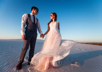 the bride and groom on the beach at sunset