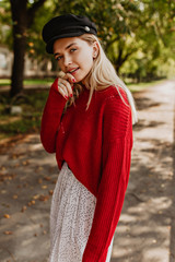 Wall Mural - Gorgeous blonde woman posing on the autumn background. Beautiful girl wearing nice black hat with red sweater and white skirt.