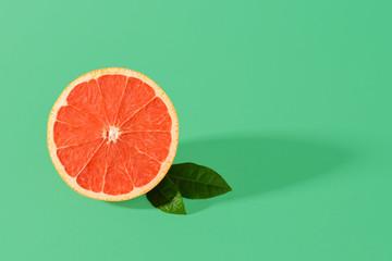 Half of ripe juicy pink grapefruit and two leaves with shadow on a green background. Organic antioxidant. Vegetarian, raw food diet and healthy eating.