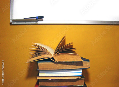 Cuadros en Lienzo Libros apilados y una pizarra con pared de fondo color amarilla