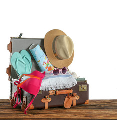 Wall Mural - Open vintage suitcase with different beach objects packed for summer vacation on wooden table against white background