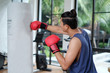 An asian sport man wearing red boxing gloves punching heavy bag at training fitness gym.