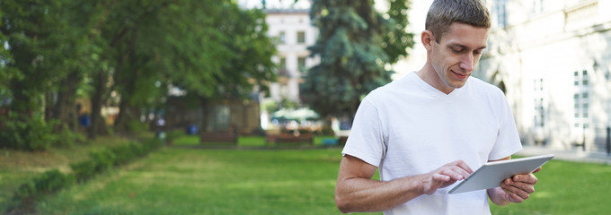 Young creative man sitting in a street and using tablet computer