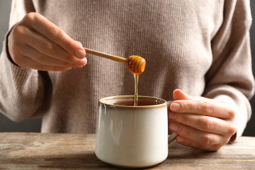 Sticker - Woman putting honey into tea at wooden table, closeup