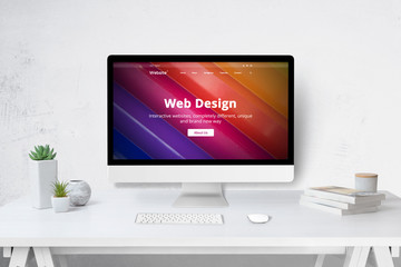 Fototapete - Web design studio concept with computer on work desk and company web site on display. White wooden desk with keyboard, mose, plants and books