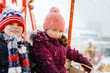 Two little kids, boy and girl having fun on ferris wheel on traditional German Christmas market during strong snowfall. Happy children enjoying family market in Germany. Lovely siblings.