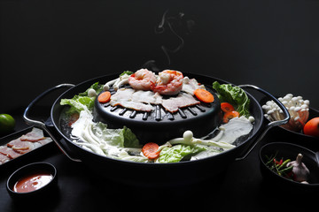 electric barbecue grill hot pot is full of shrimps , prawns , bacon , mushroom and vegetable on the black table in the  shabu restaurent