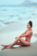 The girl sits on the sand by the sea and smile. Girl in pink swimsuit