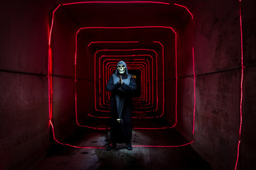 Shot of a person dressed as the grim reaper in a tunnel with red lights