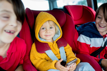 Wall Mural - Three children, boys, traveling in car in carseat and playing on mobiles