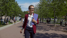 Young Smiling Businesswoman With Clipboard Walking Down City Alley