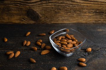 Wall Mural - Almonds in a small plate with scattered nuts of almonds around a plate on a vintage wooden table as a background. Almond is a healthy vegetarian protein nutritious food. Natural nuts snacks.