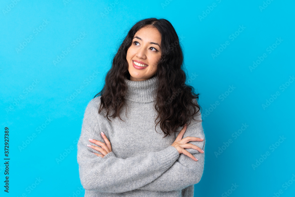 Spanish Chinese woman over isolated blue background looking up while smiling - obrazy, fototapety, plakaty 