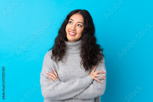 Spanish Chinese woman over isolated blue background looking up while smiling Tableau sur Toile