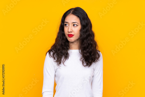 Fotografía Mixed race woman over isolated yellow background standing and looking to the sid