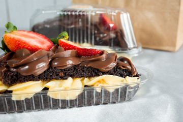 Poster - Closeup of a piece of delicious cake with a chocolate and strawberry topping in a plastic container