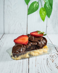 Poster - Vertical shot of a piece of cake with a chocolate and strawberry topping in a plastic container