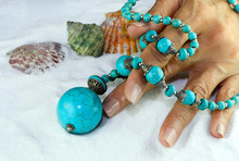 Beautiful Blue Turquoise Necklace Placed On The Woman's Hand On Clean White Sand.