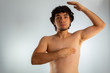 © Antonio Tanaka - Young naked hispanic man with wavy hair and shaved beard, doing a checkup on his chest for signs of breast cancer